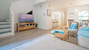 Amplia sala de estar con mueble de madera para entretenimiento, un televisor, una mesa de comedor con sillas y un rincón de estar acogedor.