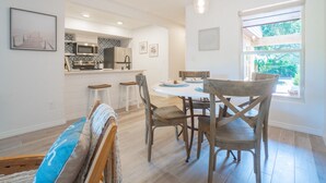Una cocina moderna con armarios blancos, un microondas y un lavamanos. Hay un comedor con una mesa redonda y sillas de madera.