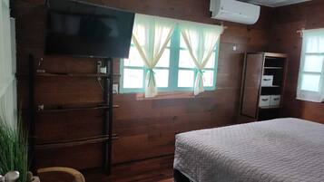 A wooden room with a bed, a TV mounted on the wall, a wardrobe, and a window with curtains.