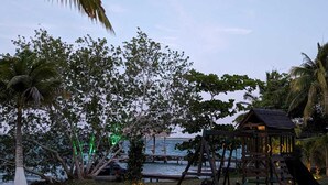 A wooden play structure with a slide and swings, surrounded by palm trees and a beach view. - Beautiful Cabin with private dock in Bacalar Lake (Buenavista)