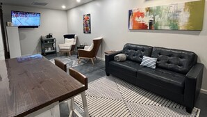 Un salon moderne avec un canapé en cuir foncé, une table à manger en bois et un téléviseur à écran plat fixé au mur.