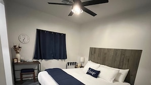 Une chambre bien rangée, avec un lit, un bureau, une chaise, une horloge et un ventilateur de plafond.