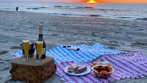 Een picknick op het strand, compleet met champagnefles, een glas sinaasappelsap en een picknickmand op een deken.