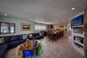 A spacious living area with a dark-colored sofa, a wooden dining table, and a kitchen in the background.