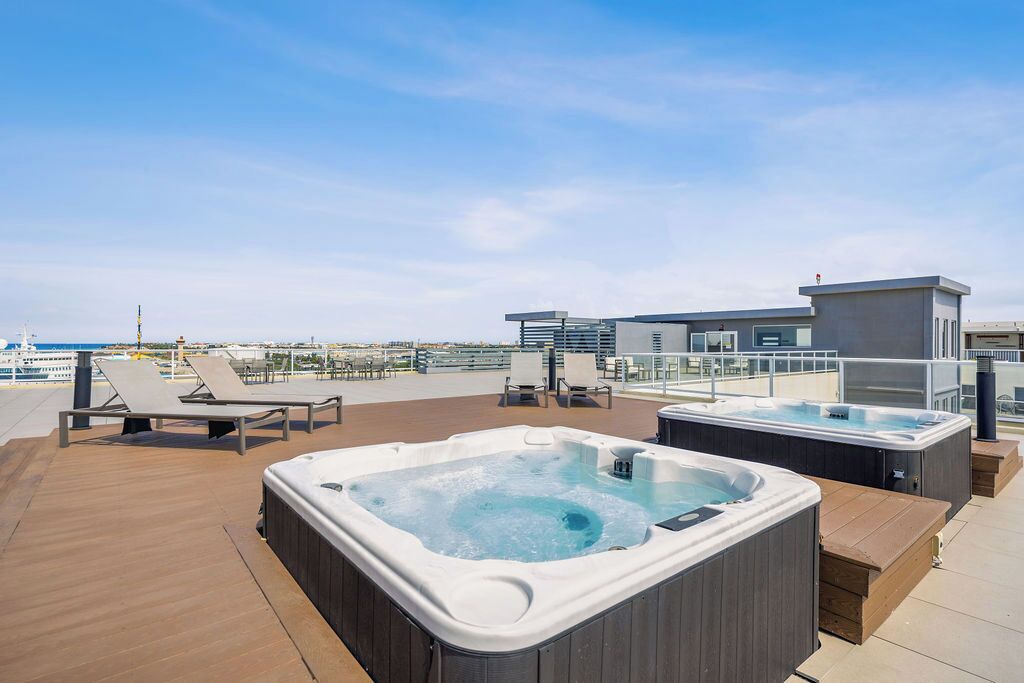 A rooftop deck with two hot tubs, lounge chairs, and a view of the sea.