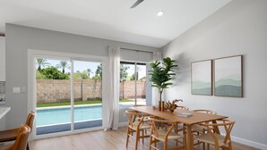 Ein geräumiger Essbereich mit Holztisch und Stühlen, einem großen Fenster mit Blick auf Pool und Grünflächen sowie einem Deckenventilator.