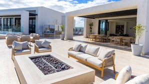 A modern outdoor lounge area with wicker furniture, a fire pit, and a view of the city.
