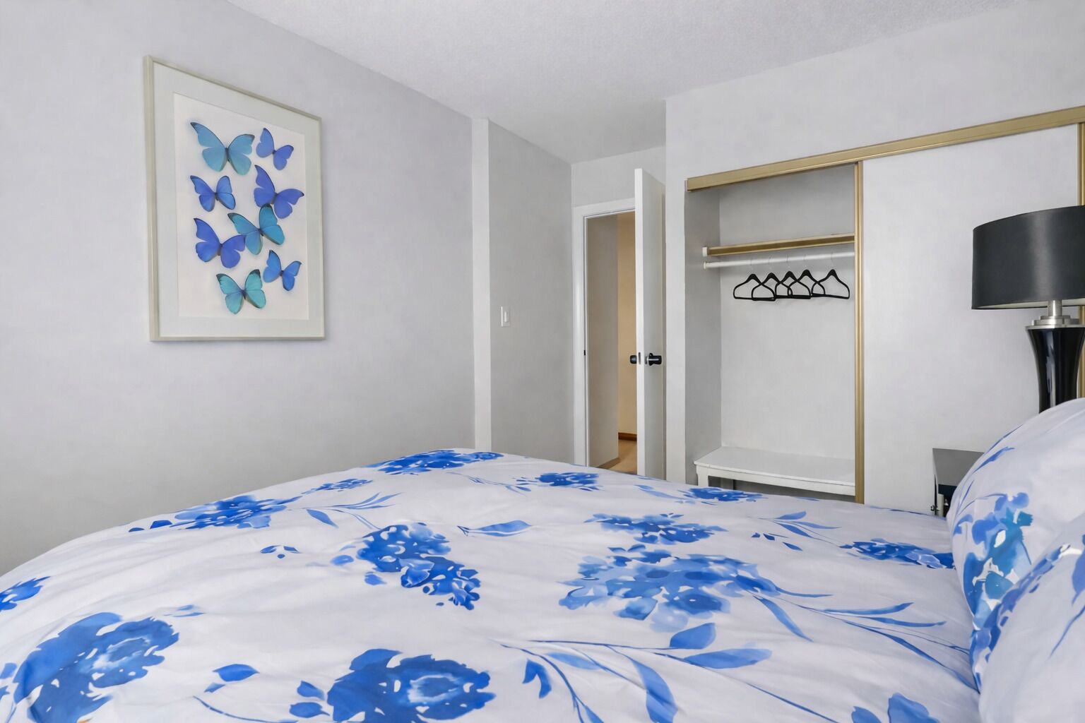 A bedroom with a bed, a framed butterfly artwork, a wardrobe, and a lamp.