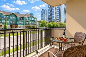 A balcony with a table set for dining, a chair, and a view of a street with buildings.