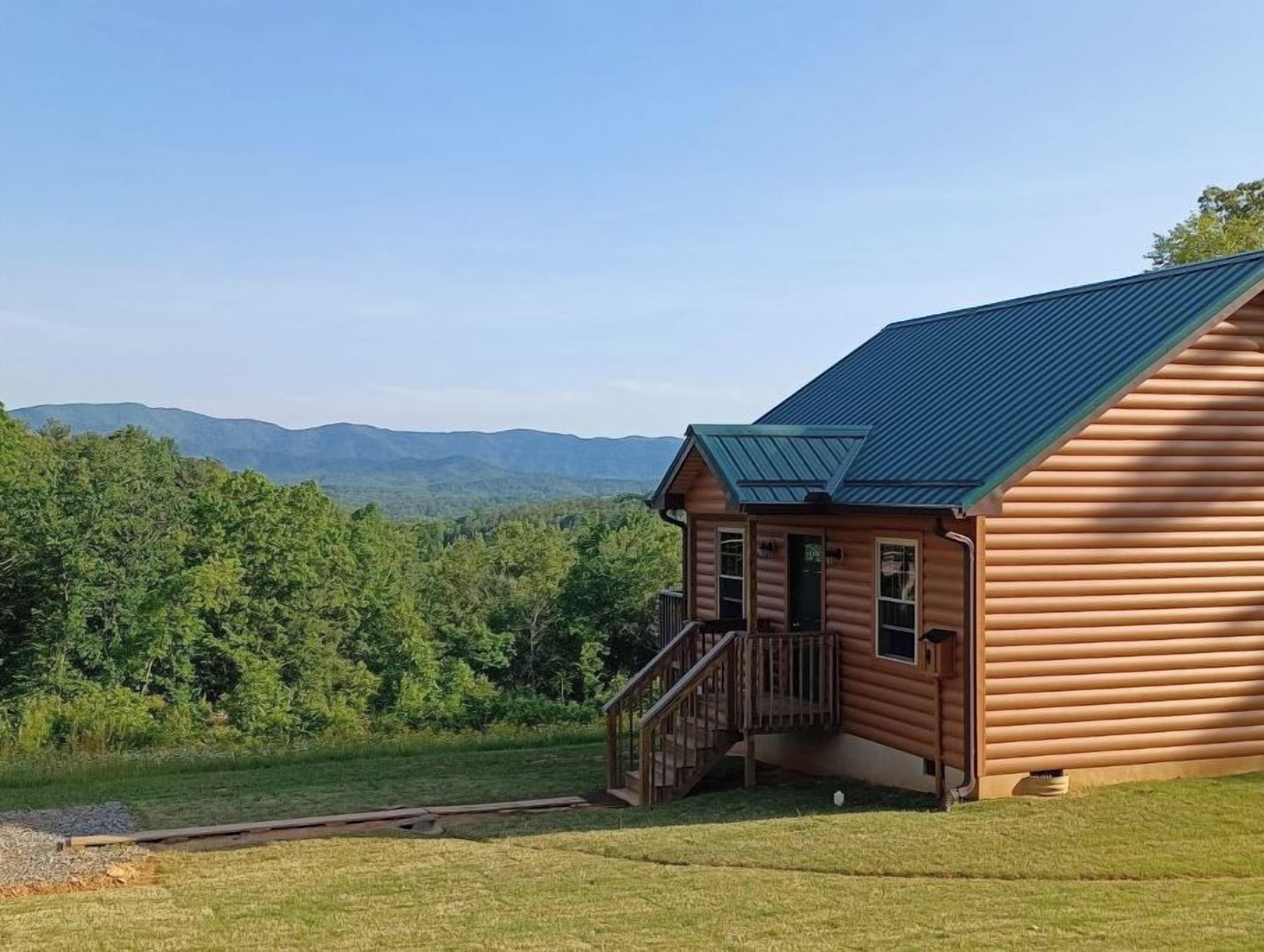 Une cabane en rondins avec un toit en métal, une terrasse en bois et une vue sur une chaîne de montagnes boisées.