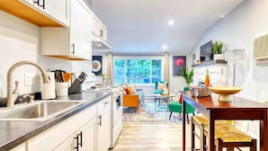 Una cocina moderna con armarios blancos, un lavamanos de acero inoxidable y un comedor con una mesa y sillas de madera.