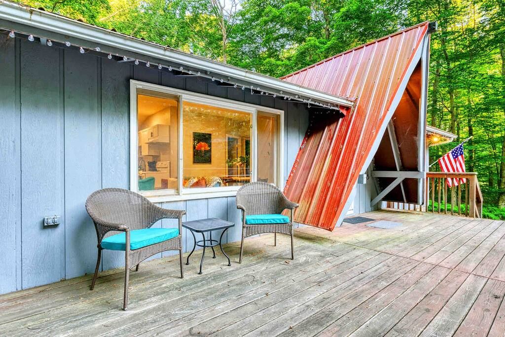 A rustic cabin with a porch, two wicker chairs, a small table, and a wooden deck.