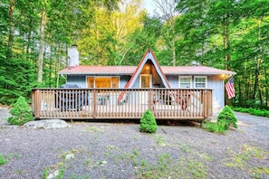 A cabin with a wooden deck, a chimney, and an American flag.