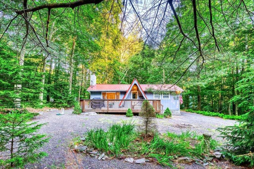A cabin with a red roof and a porch, surrounded by dense forest.