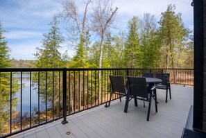 Eine Holzterrasse mit Tisch und Stühlen mit Blick auf einen See, umgeben von Bäumen.