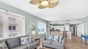 A spacious living room with a grey sofa set, a dining area with white chairs, and a kitchen in the background. - 🌞Beachfront|Gulf Views|Pools|3BR Summerwind 804🌞 (Navarre Beach)