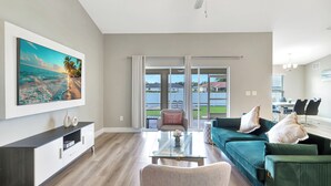 Een ruime woonkamer met een groot raam, een plafondventilator, een flatscreen-televisie aan de muur en een groene bank met decoratieve kussens.