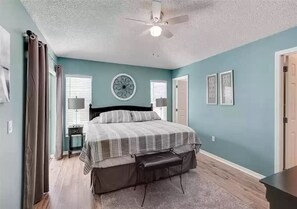 Une chambre à coucher avec un lit, un ventilateur de plafond, une fenêtre avec des stores et une porte.