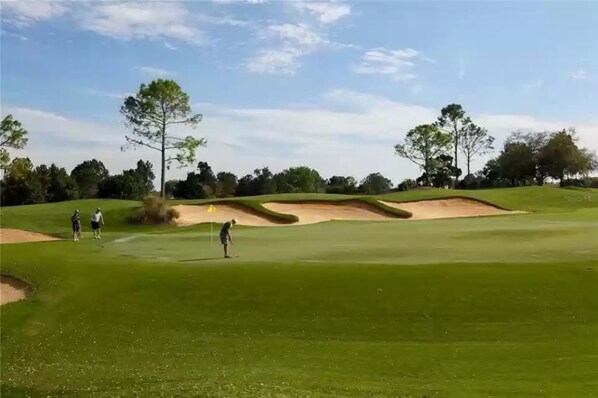 Um campo de golfe com bunkers de areia, árvores e céu claro.