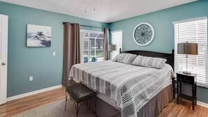Un dormitorio con cama, ventilador de techo, ventana con persianas, una silla y un reloj de pared.