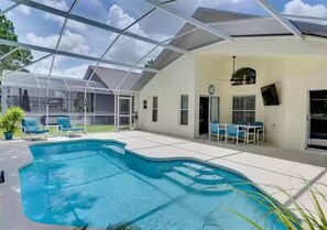Piscina descoberta coberta por uma estrutura de vidro, rodeada por espreguiçadeiras e um espaço de estar ao ar livre.