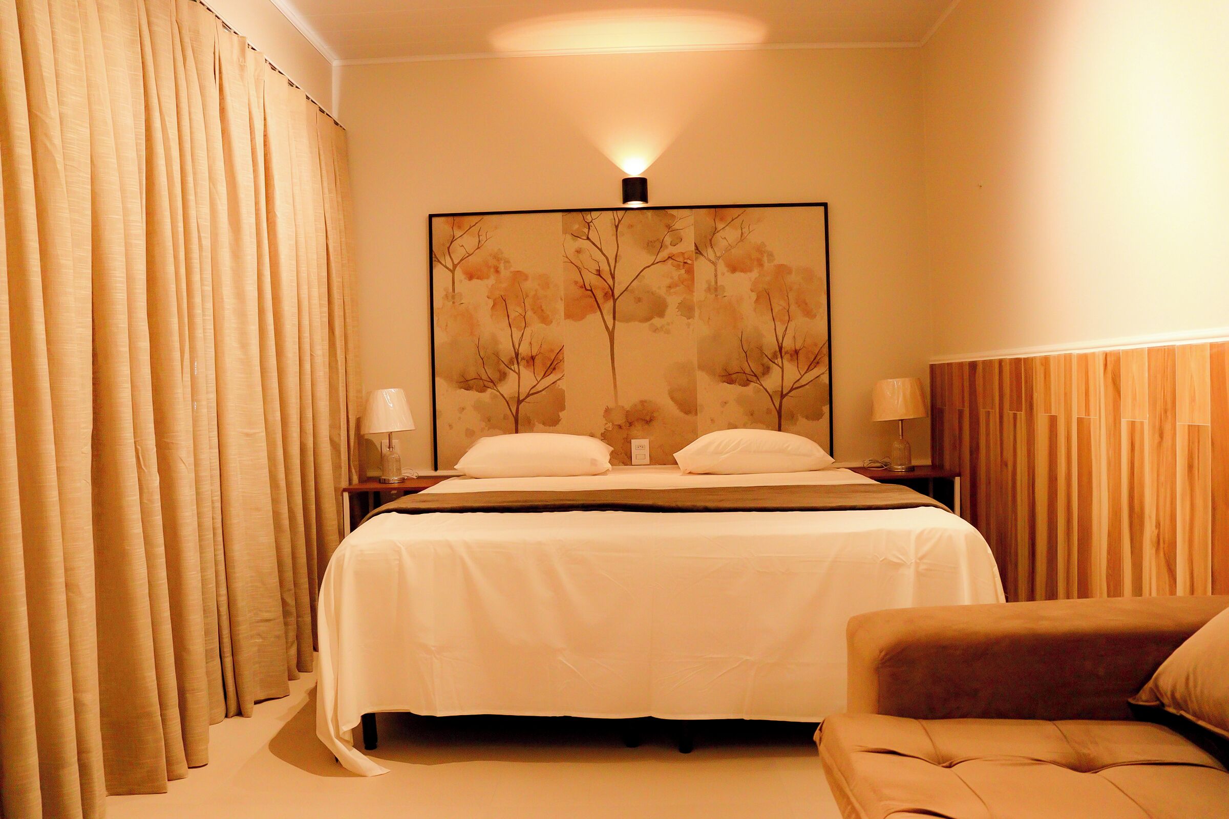 A hotel room with a bed, two bedside lamps, a large framed artwork on the wall, and a sofa.
