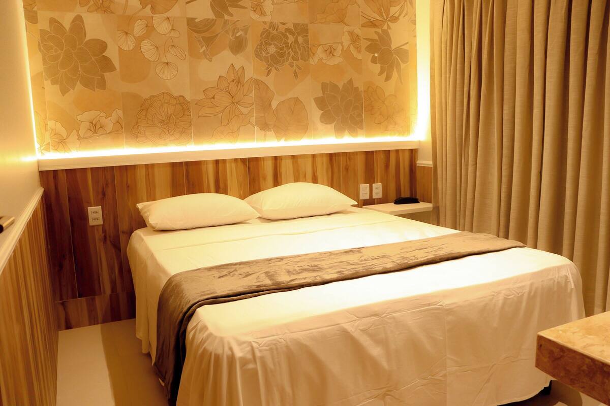 A hotel room with a bed, wooden paneling, a floral-patterned wall, and a curtain.