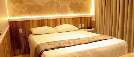 A hotel room with a bed, wooden paneling, a floral-patterned wall, and a curtain.