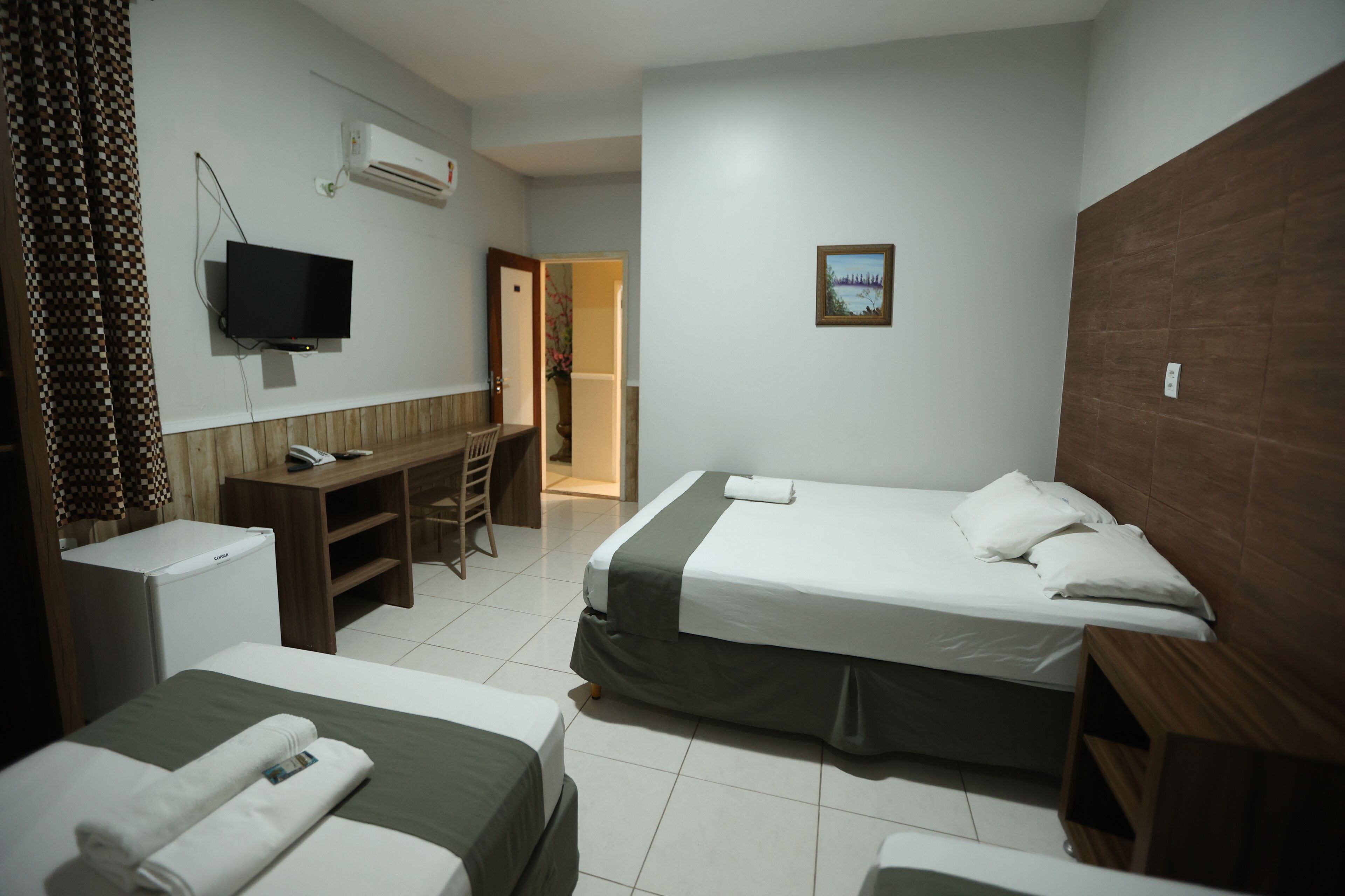 Quarto de hotel com duas camas, uma escrivaninha, televisão e um pequeno frigorífico.