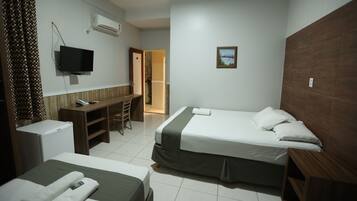 Quarto de hotel com duas camas, uma escrivaninha, televisão e um pequeno frigorífico.