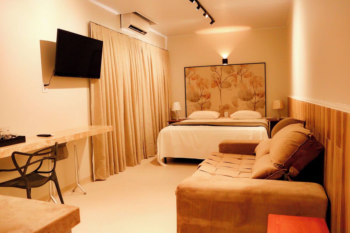 A hotel room with a bed, a desk, a chair, a TV mounted on the wall, and a painting on the wall.