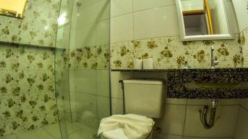 Een badkamer met een glazen douchecabine, toilet, wastafel met spiegel erboven en een betegelde muur met een bloemenmotief.