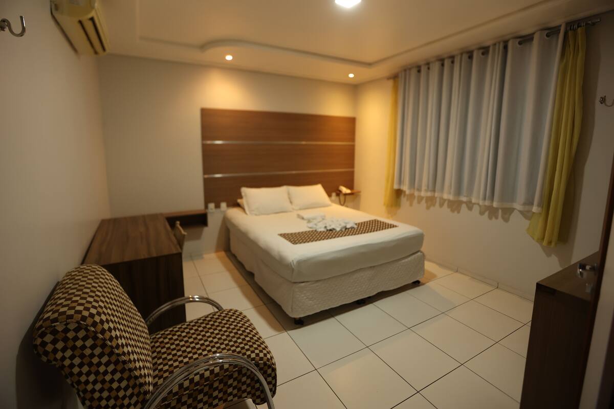 A hotel room with a bed, a desk, two chairs, and a window with curtains.