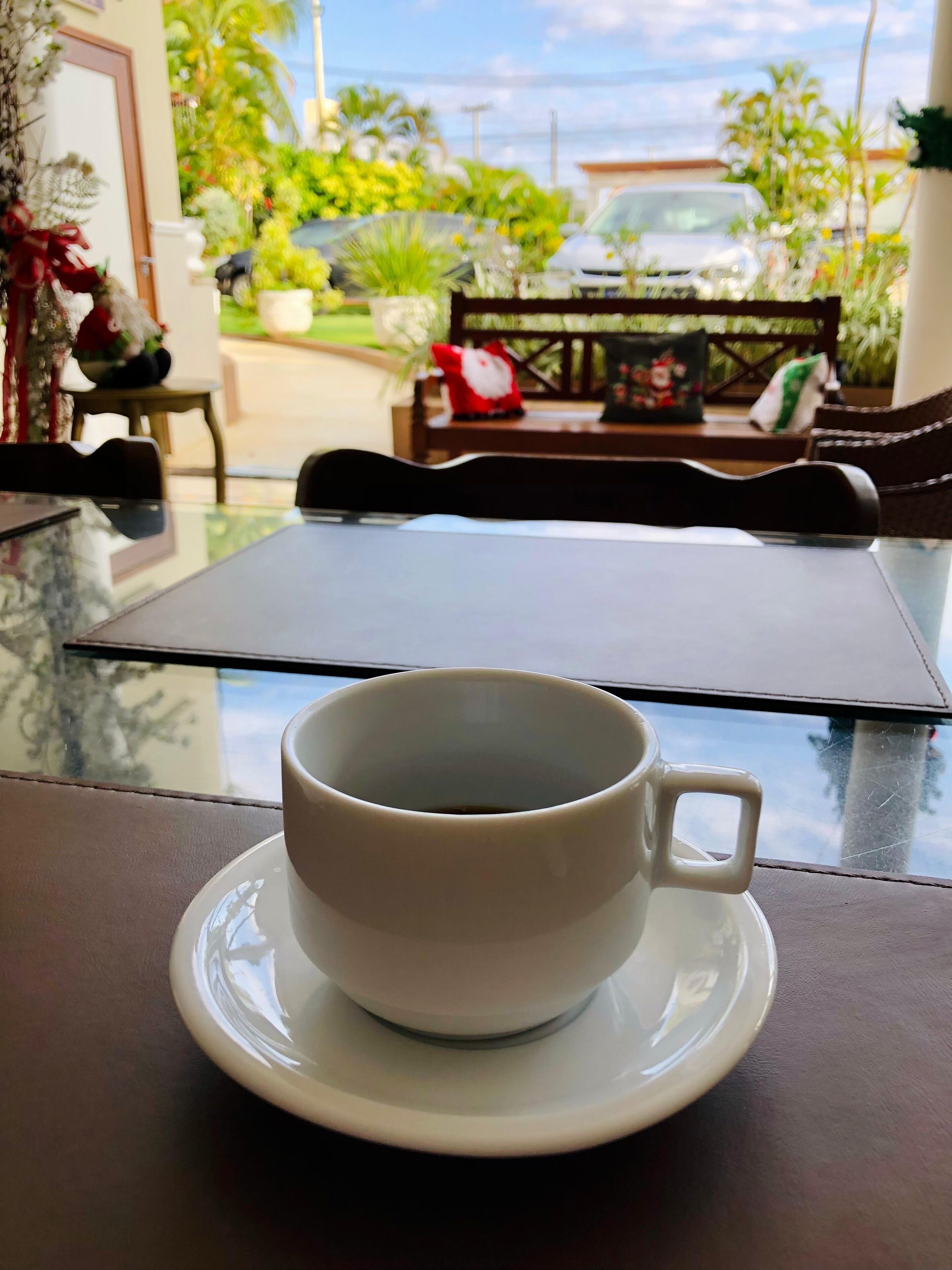 A cup of coffee on a table with a view of a garden and a bench.
