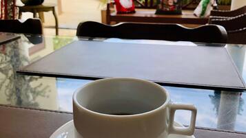A cup of coffee on a table with a view of a garden and a bench.
