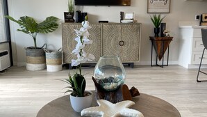 Un salon avec une table basse ronde en bois, une plante en pot, un vase décoratif en verre et un bibelot en forme d’étoile de mer.