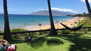 Une plage avec un hamac, une poussette et une vue dégagée sur l’océan, avec une montagne en arrière-plan.