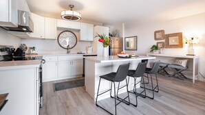 Une cuisine moderne avec des meubles blancs, un îlot central doté de tabourets, un four encastré et un réfrigérateur en acier inoxydable.