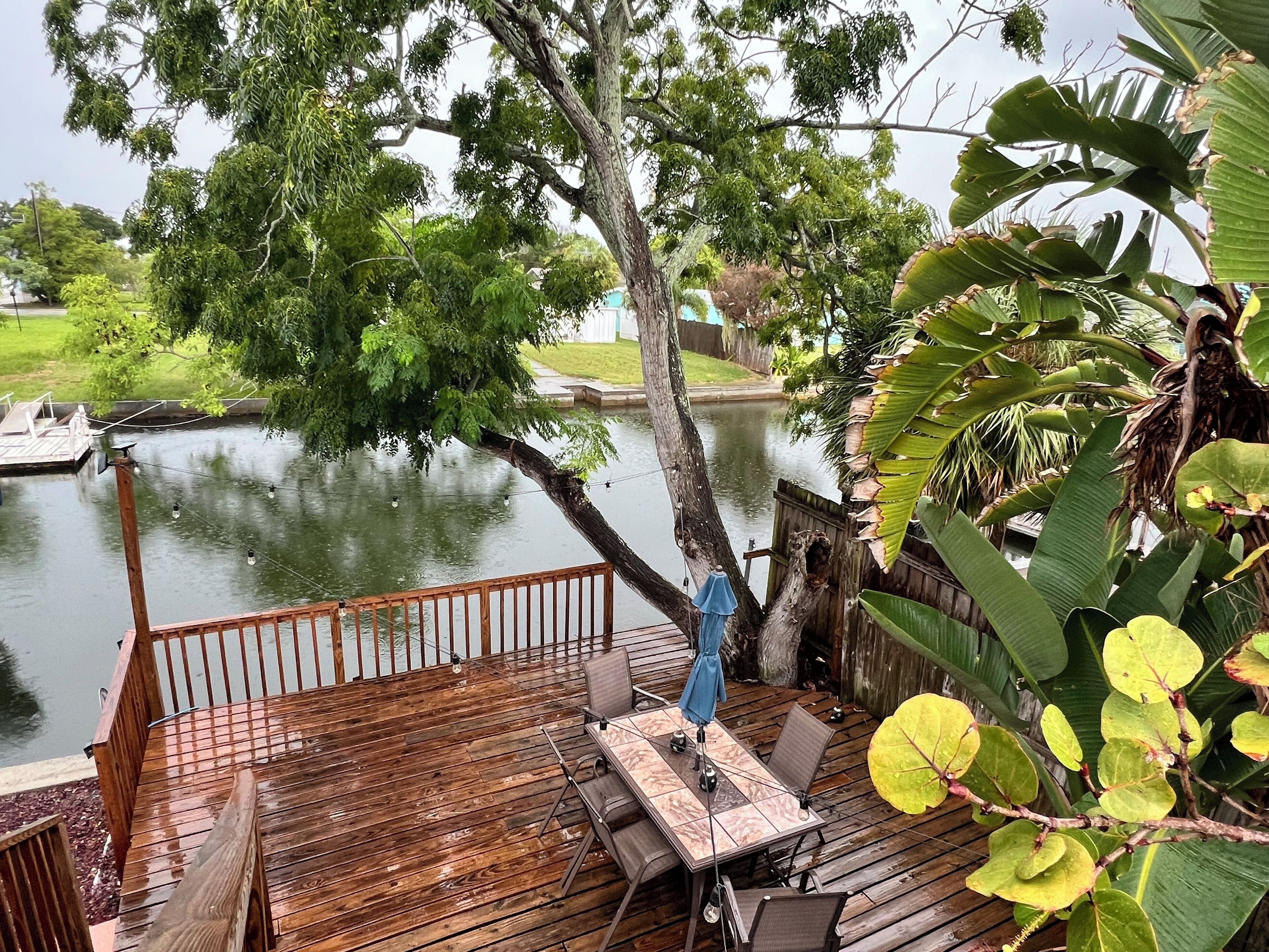 A wooden deck with a table and chairs, overlooking a body of water and a grassy area.