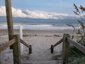 Una escalera de madera que baja a una playa arenosa con el océano al fondo.