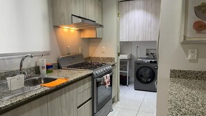 A modern kitchen with granite countertops, a stainless steel sink, a built-in oven, and a washing machine in the adjacent room. - Condo en Residencial con Alberca (Durango)