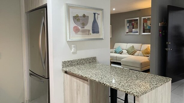 A modern kitchen with a built-in island, stainless steel refrigerator, and a dining area with a sofa and cushions. - Condo en Residencial con Alberca (Durango)