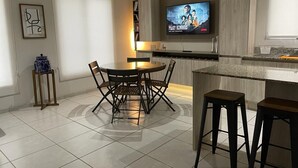 A modern kitchen with a dining area, a TV mounted above the counter, and a small side table with a vase. - Condo en Residencial con Alberca (Durango)