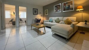 A modern living room with a sofa, coffee table, and chairs. There are framed pictures on the wall and a lamp on a side table. - Condo en Residencial con Alberca (Durango)
