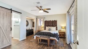 Une chambre à coucher avec un lit, un ventilateur de plafond, une table de chevet, une lampe et une porte.