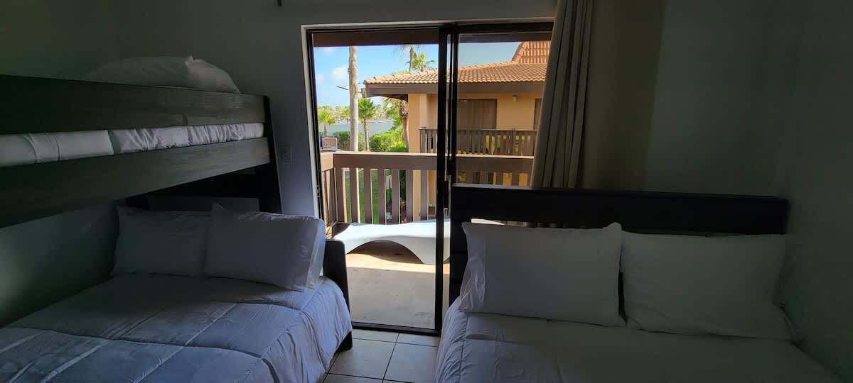 A hotel room with two beds, a balcony, and a view of a building with a tiled roof.