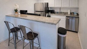 Une cuisine avec des meubles blancs, des appareils en acier inoxydable, un comptoir en granit et deux tabourets de bar.