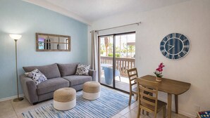 Un salon comprenant un canapé, des poufs, une table, des chaises, une horloge et une fenêtre donnant sur un beau paysage.