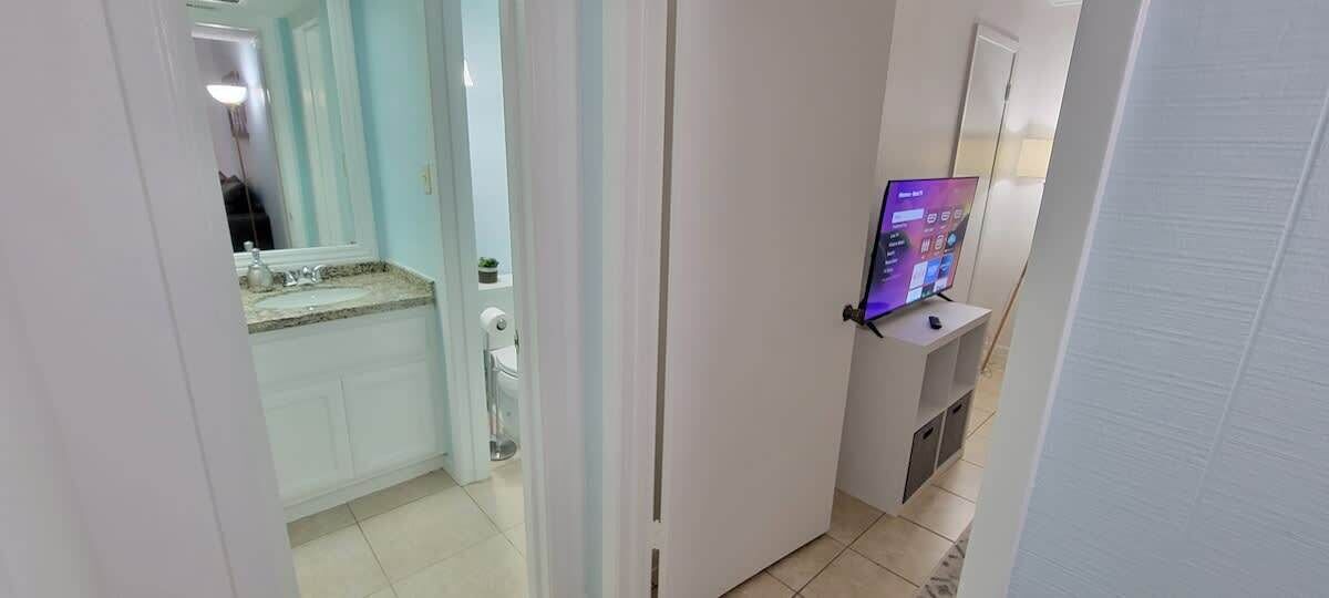 Un pasillo con un baño a la izquierda, un televisor a la derecha y una puerta al final.
