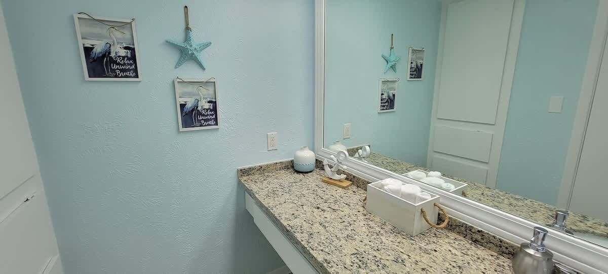 Un baño con encimera de granito, un espejo grande y decoraciones de estrellas de mar en la pared.